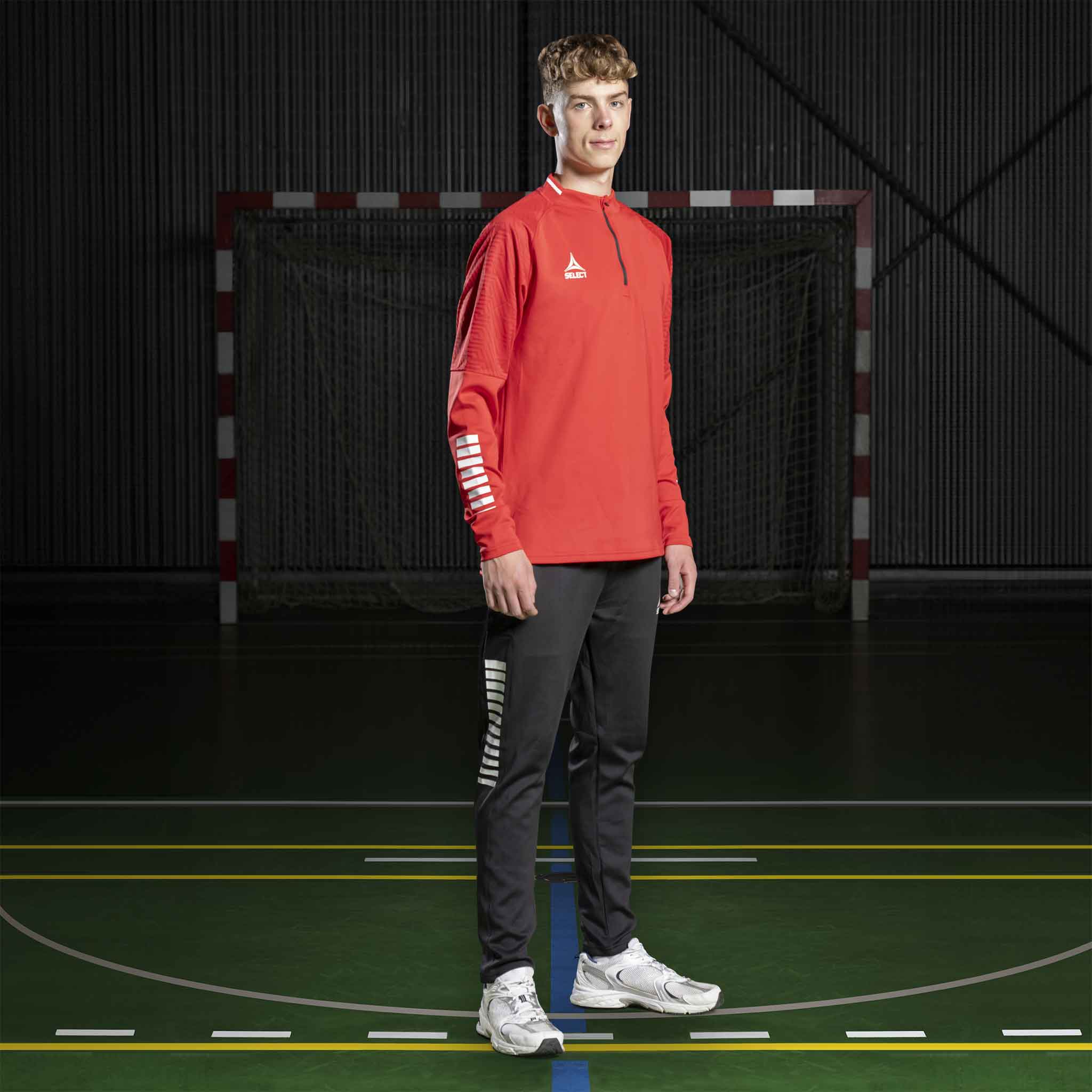 Mandlig håndboldspiller i rød Training sweat 1/2 zip Monaco v24 og sorte bukser, Match & Training wear, på banen.