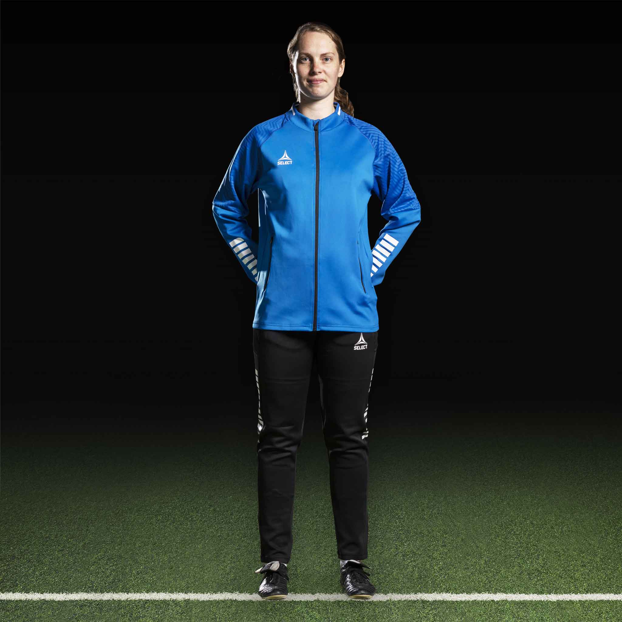 Kvindelig fodboldspiller i blå Zip jacket Monaco v24 og sorte bukser, Match & Training wear, set forfra.