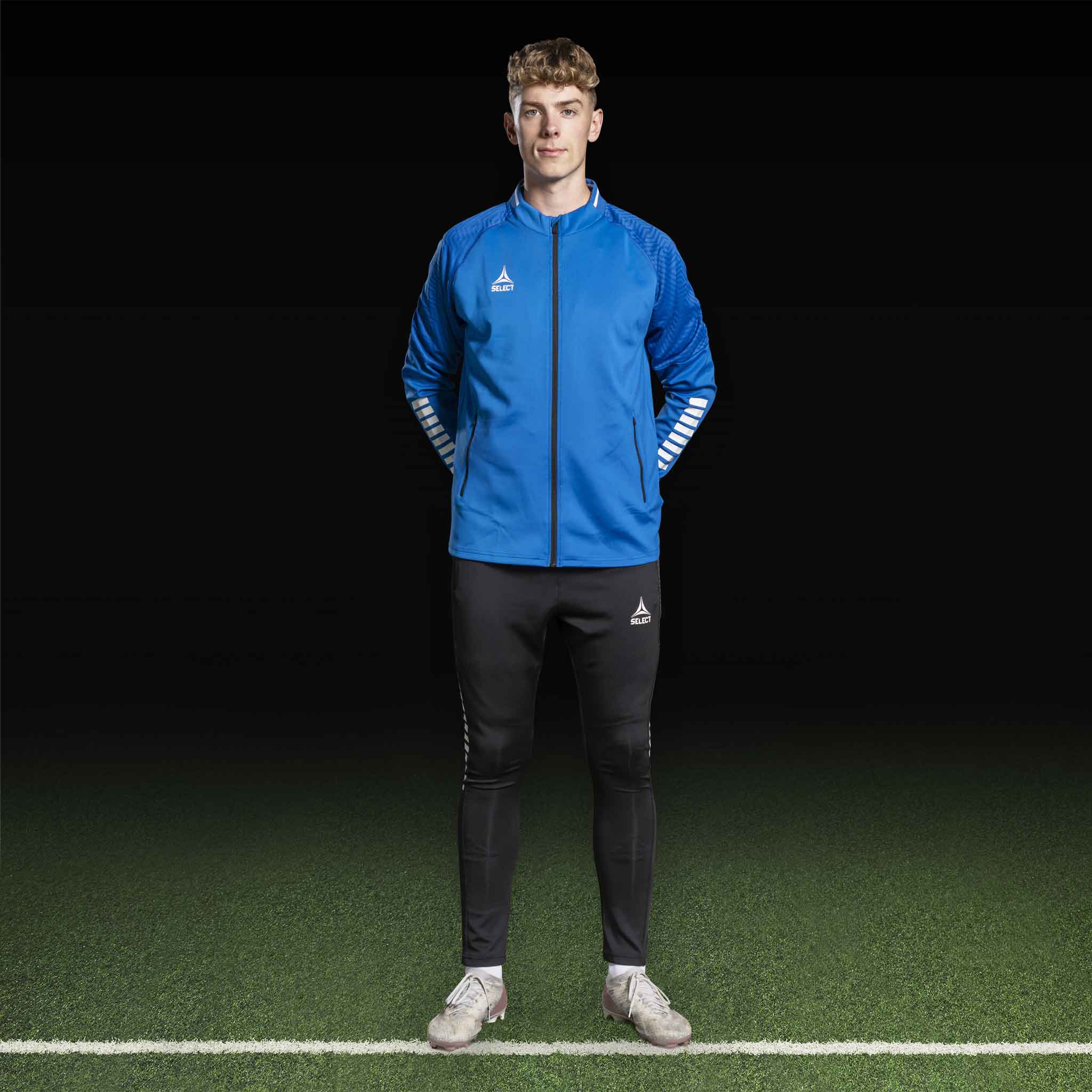 Mandlig fodboldspiller i blå/hvid Zip jacket Monaco v24 og sorte bukser, Match & Training wear.