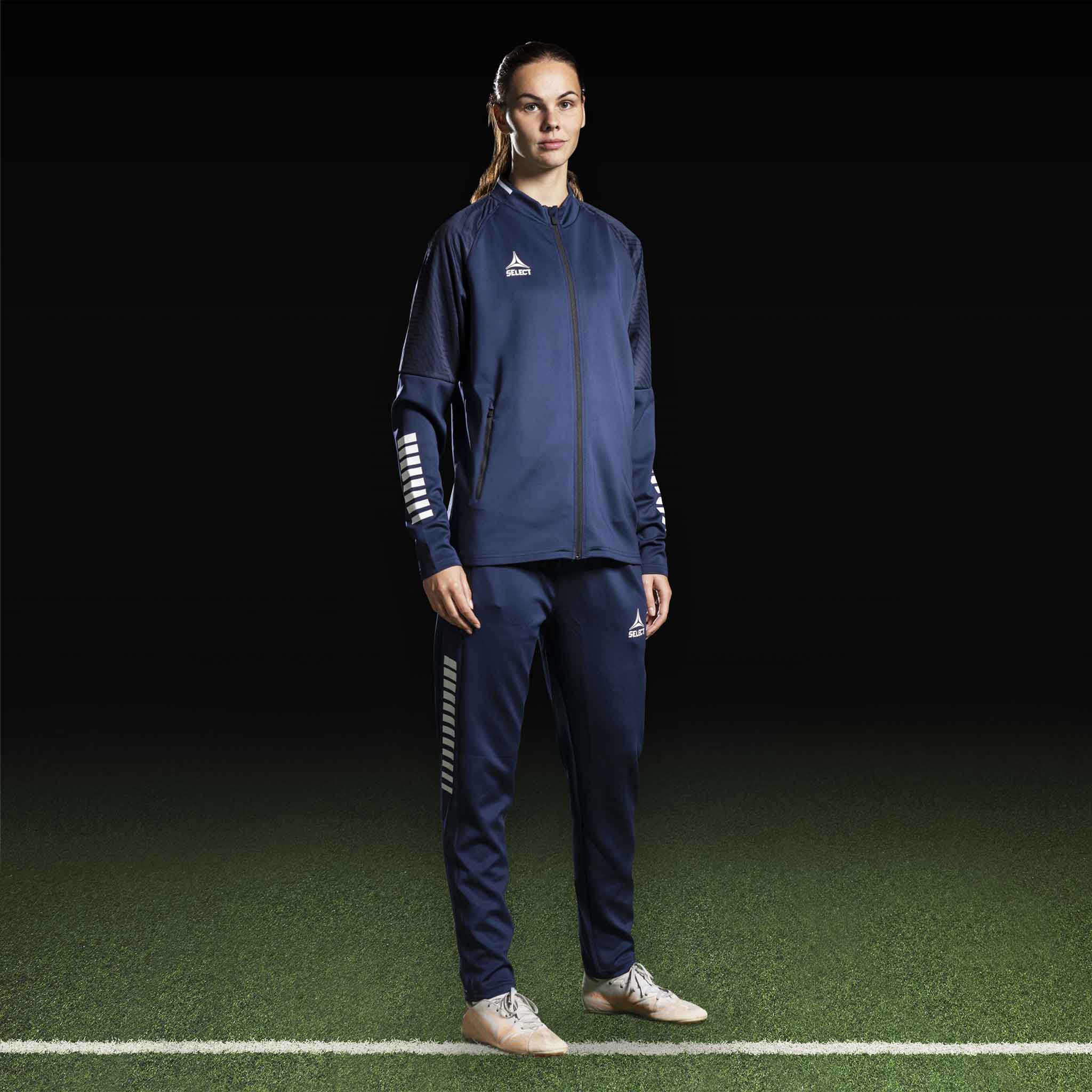 Kvindelig fodboldspiller i navy og hvid Zip jacket Monaco v24, Match & Training wear, forfra på banen.