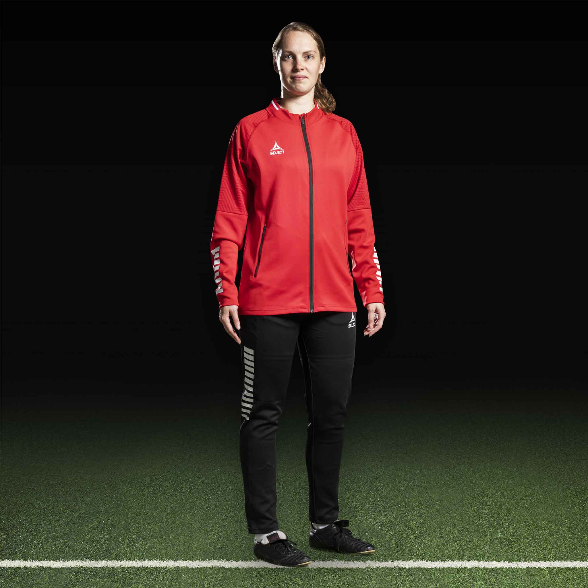 Kvindelig fodboldspiller i rød Zip jacket Monaco v24 og sorte bukser, Match & Training wear, set forfra.