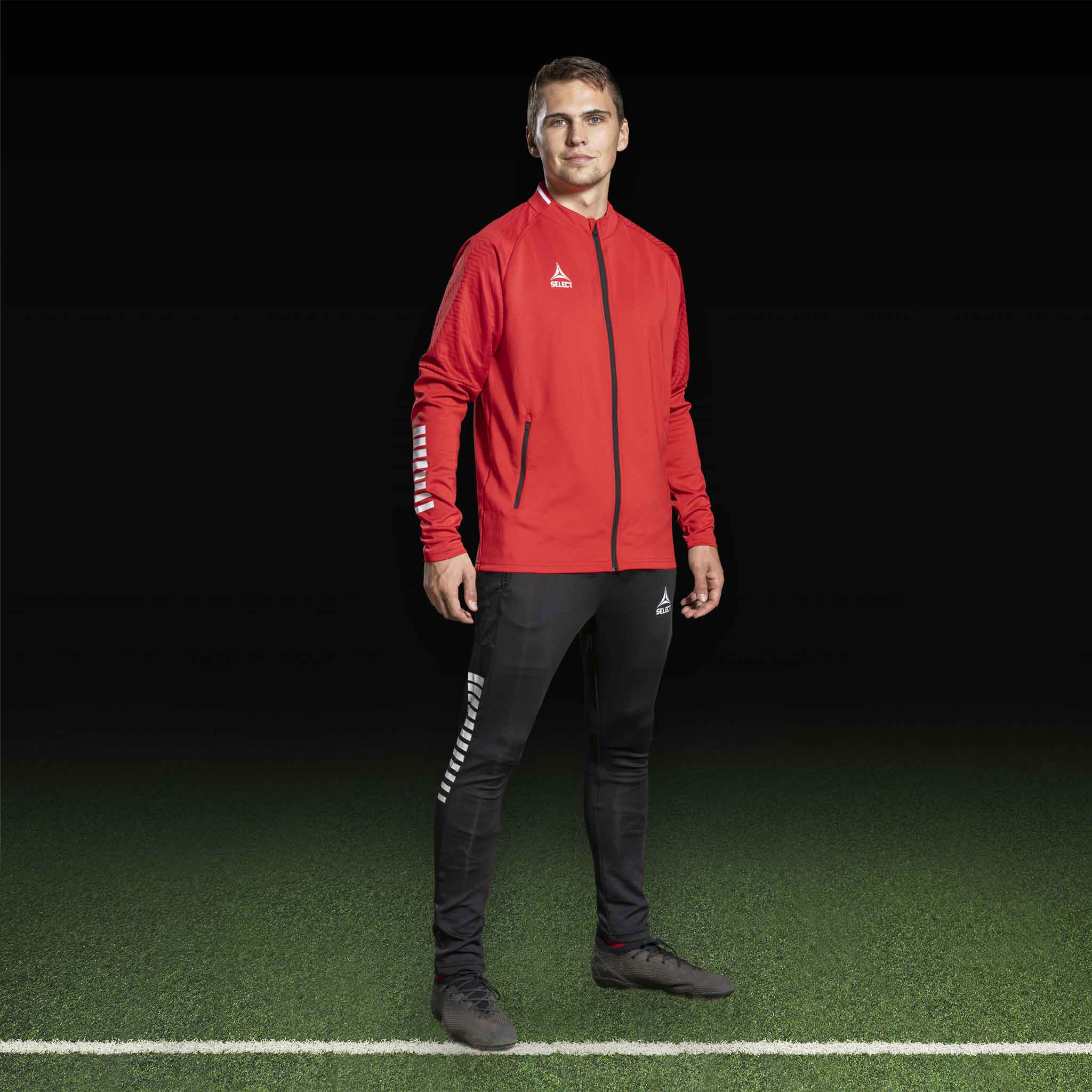 Mandlig fodboldspiller i rød Zip jacket Monaco v24 og sorte slim fit bukser, Match & Training wear.