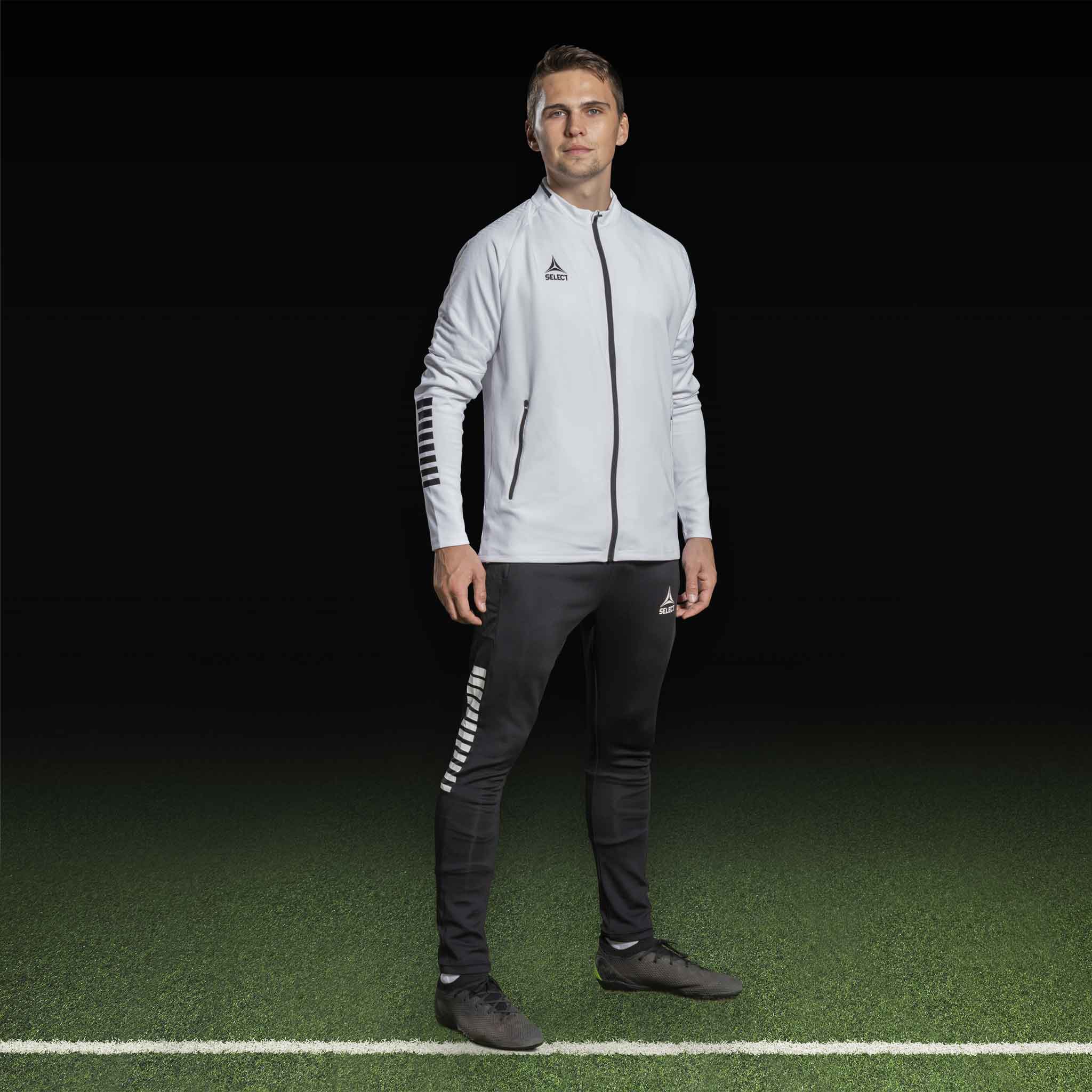 Mandlig fodboldspiller i hvid Zip jacket Monaco v24 og sorte bukser, Match & Training wear.