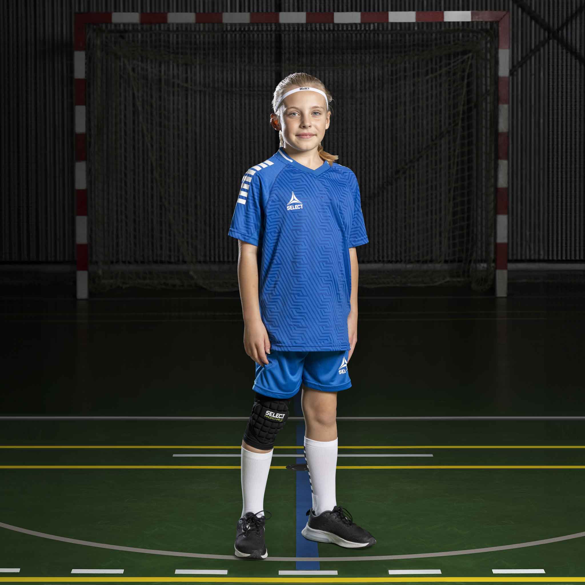 Pige håndboldspiller i blå og hvide Player shorts Monaco v24, Match & Training tøj, forfra på banen.