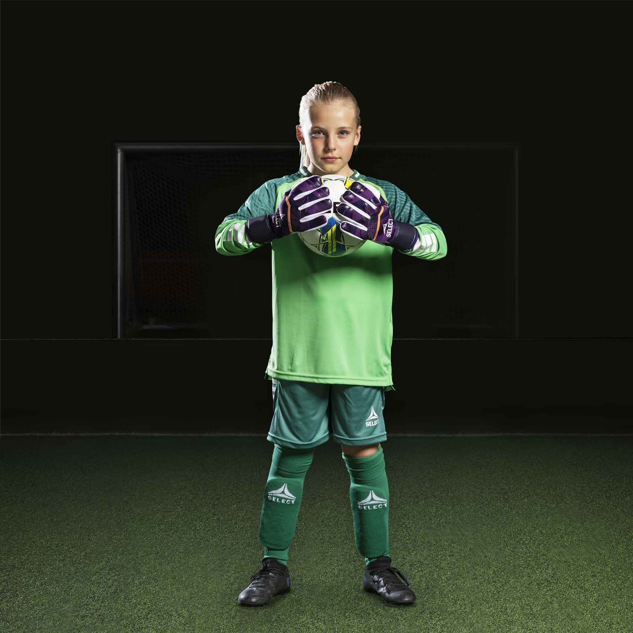 Ung fodboldspiller iført grøn Goalkeeper shirt Monaco v24, målmandstøj, med matchende handsker og shorts.