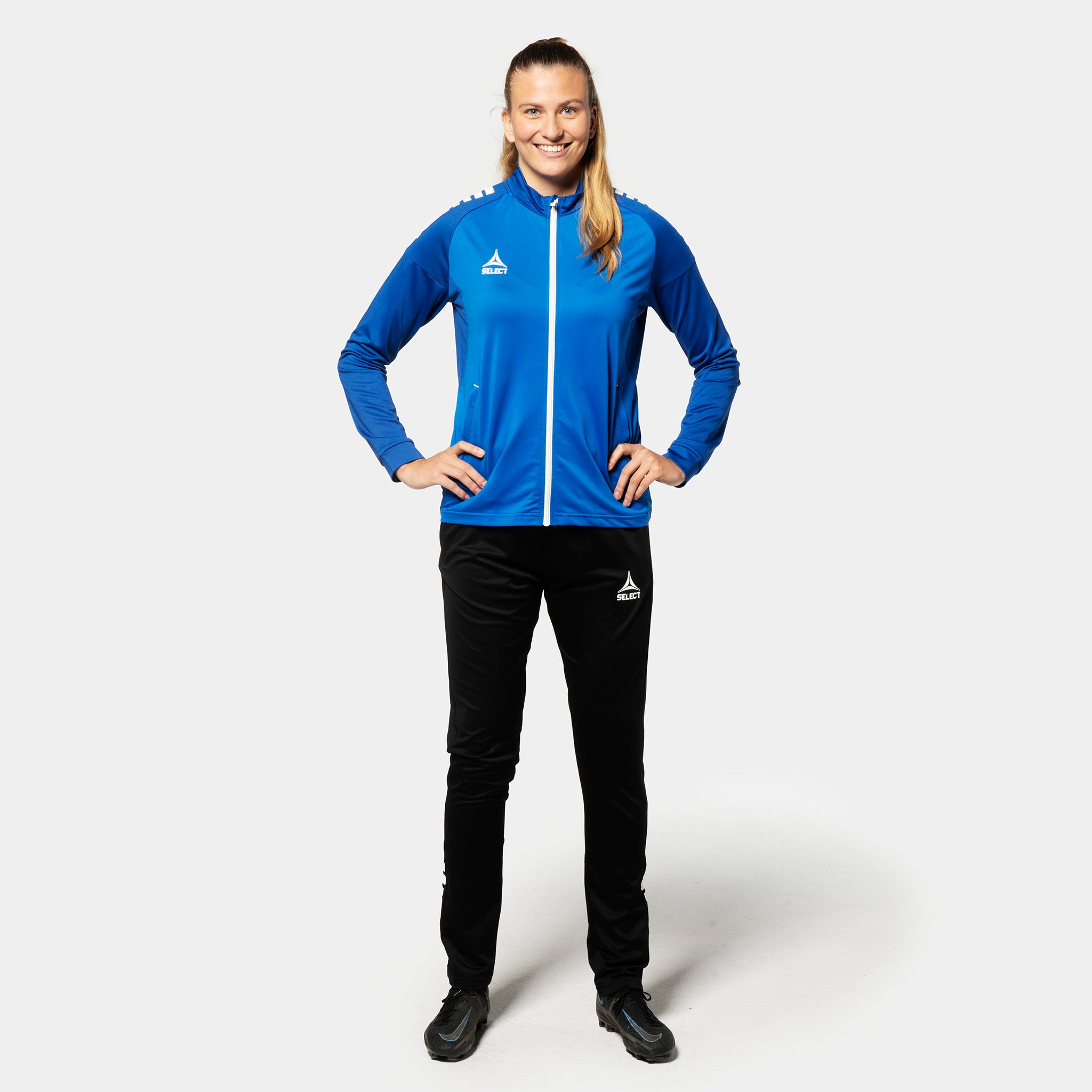 Kvindelig fodboldspiller i blå-hvid Training zip jacket Spain woman v25, Match & Training tøj, med sorte bukser, set forfra.