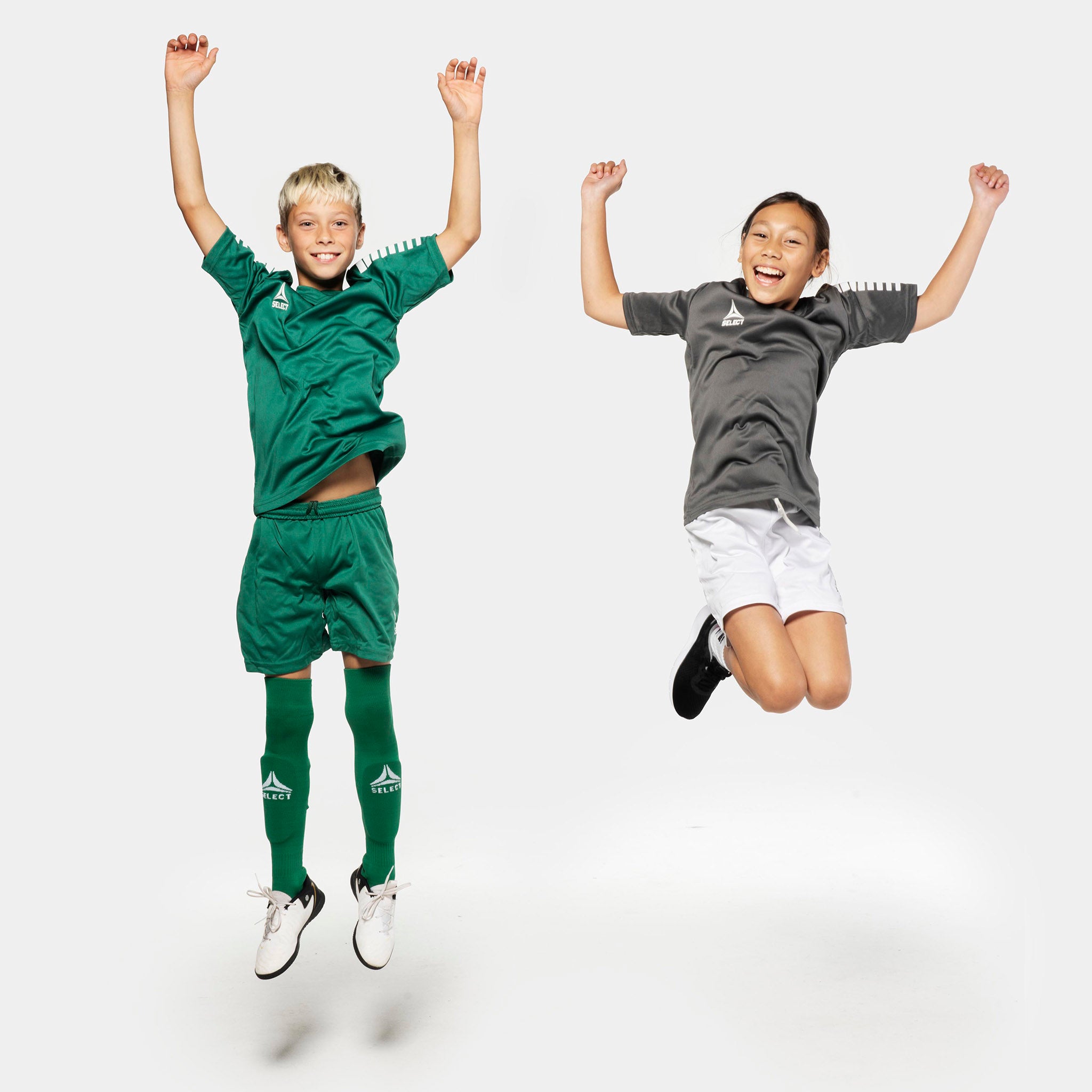 Dreng og pige fodboldspillere hopper i Pisa spillershorts, Match & Training tøj, i grøn og hvid.