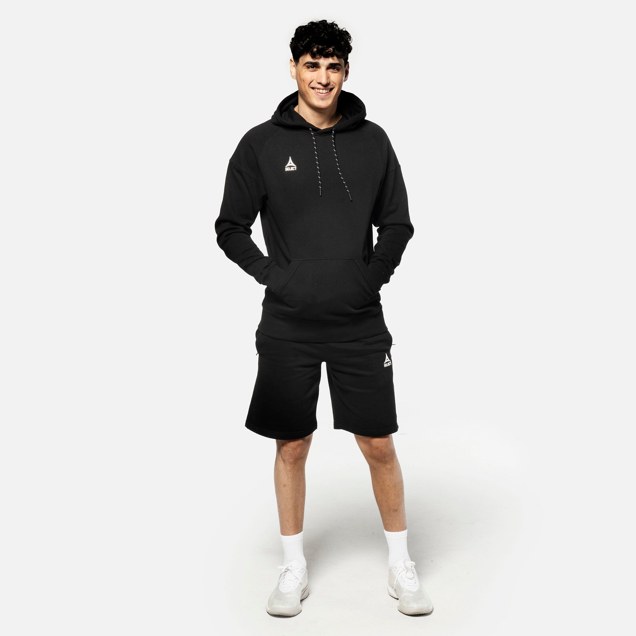 Mandlig fodboldspiller i sorte Sweat shorts Oxford v25 og sort hoodie, fritidstøj, forfra.