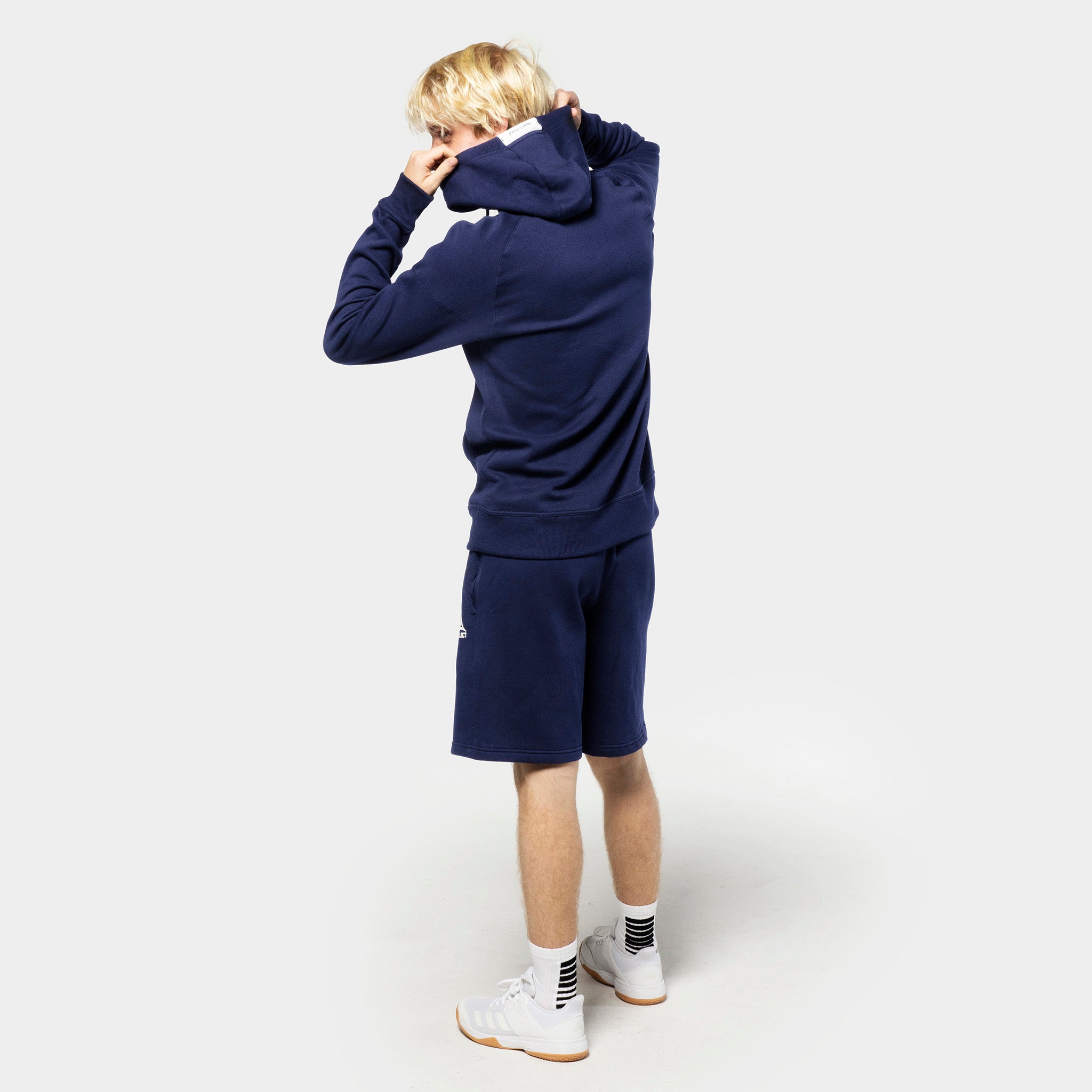 Bagfra af mandlig fodboldspiller i marineblå Sweat shorts Oxford v25 og matchende hættetrøje, fritidstøj.