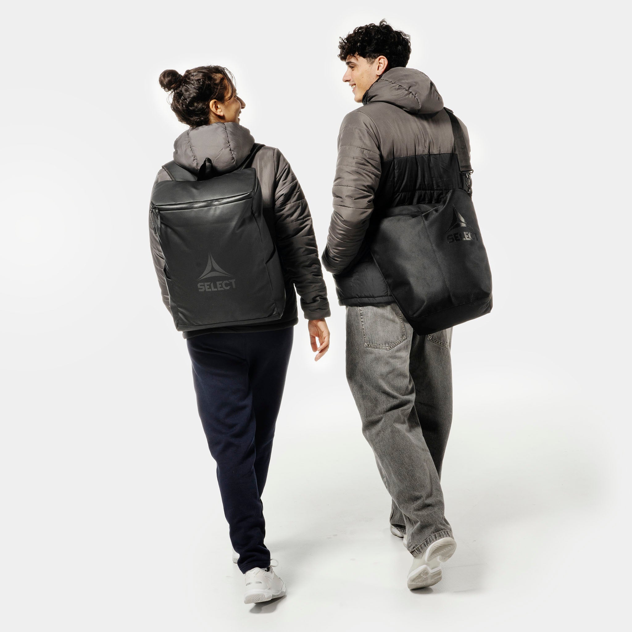 Kvinde og mand fodboldspillere med sorte Crossbody v25 sportstasker, set bagfra.